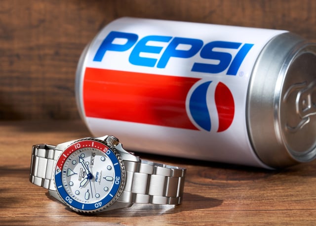 watch next to a pepsi can on wood surface