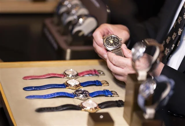 A guest examines a wristwatch beside several luxury watches displayed on colorful leather straps.